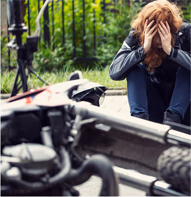 Injured rider sitting near fallen motorcycle after motorcycle accident.